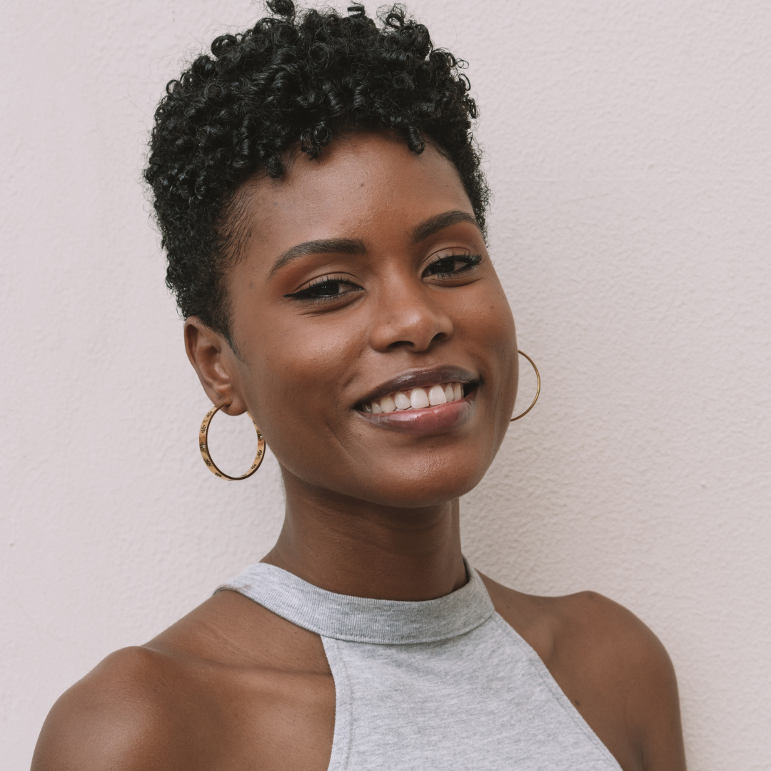 Woman with short curly hair wearing a gray sleeveless top against a light background